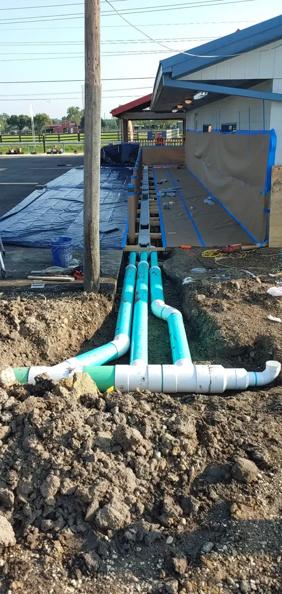 Parallel green drain pipes joined into a white header pipe beside a building under construction