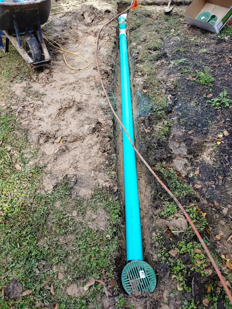 Green drain pipe with a round green grate fitting lying in a trench