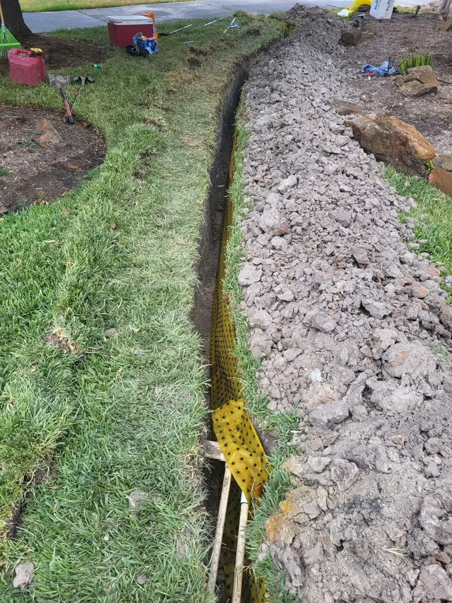 Trench filled with crushed rock alongside a lawn, with drainage fabric at the edge
